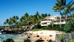A large white home with a wraparound porch on a palm tree-covered beach in Hawaii
