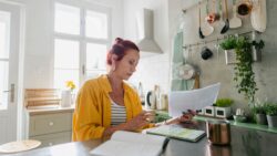 Woman sits in her brightly lit modern kitchen looking at refinance paperwork