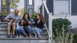 A young happy family sits on the front steps of their newly purchased home